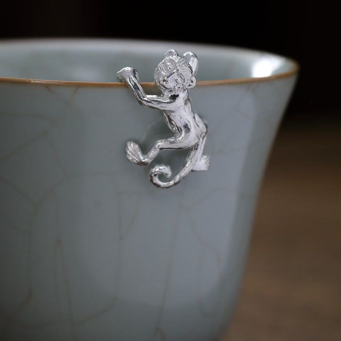 Silver monkey charm on a ceramic cup with a dark background