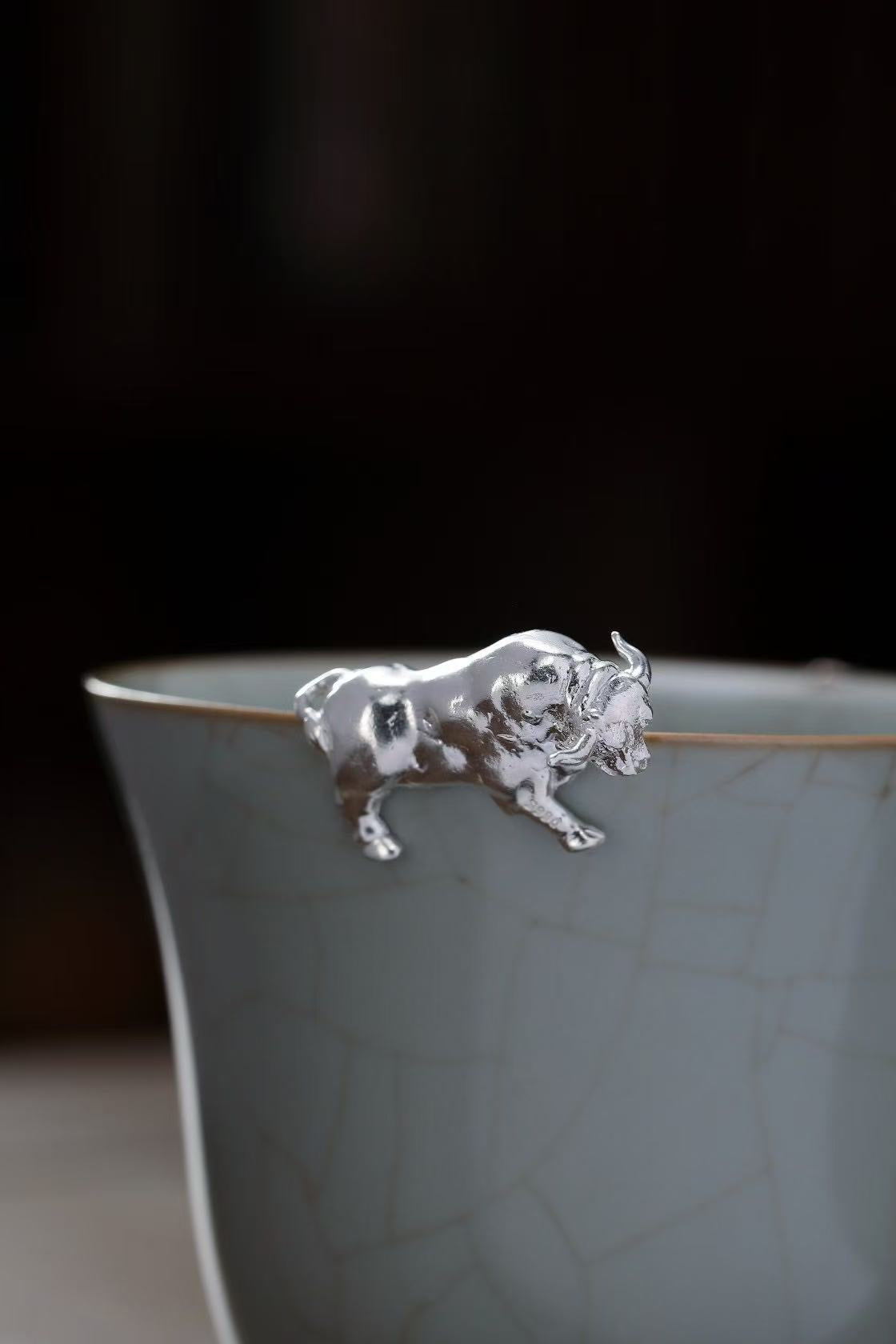 Silver bull-shaped object on a ceramic cup with a dark background